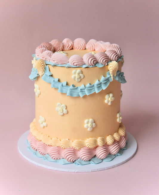 A multi-layered cake with beige, blue, and pink icing, decorated with white flowers andlemon yellow centers